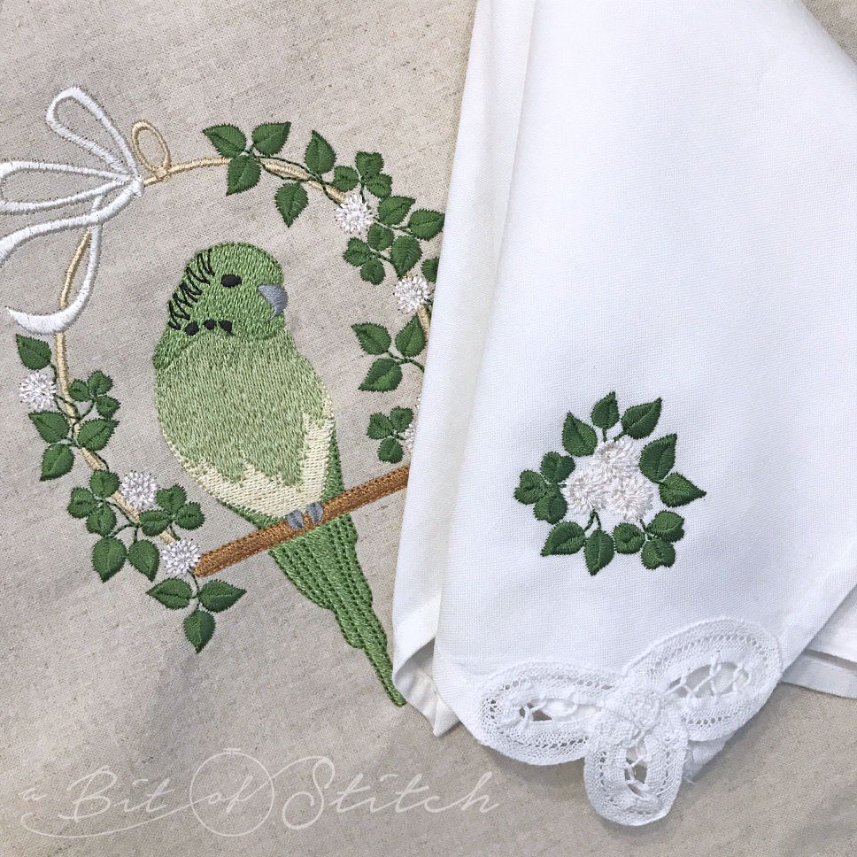 Tea towel with March Parakeet and napkin with tiny clover flower bouquet machine embroidery designs by A Bit of Stitch