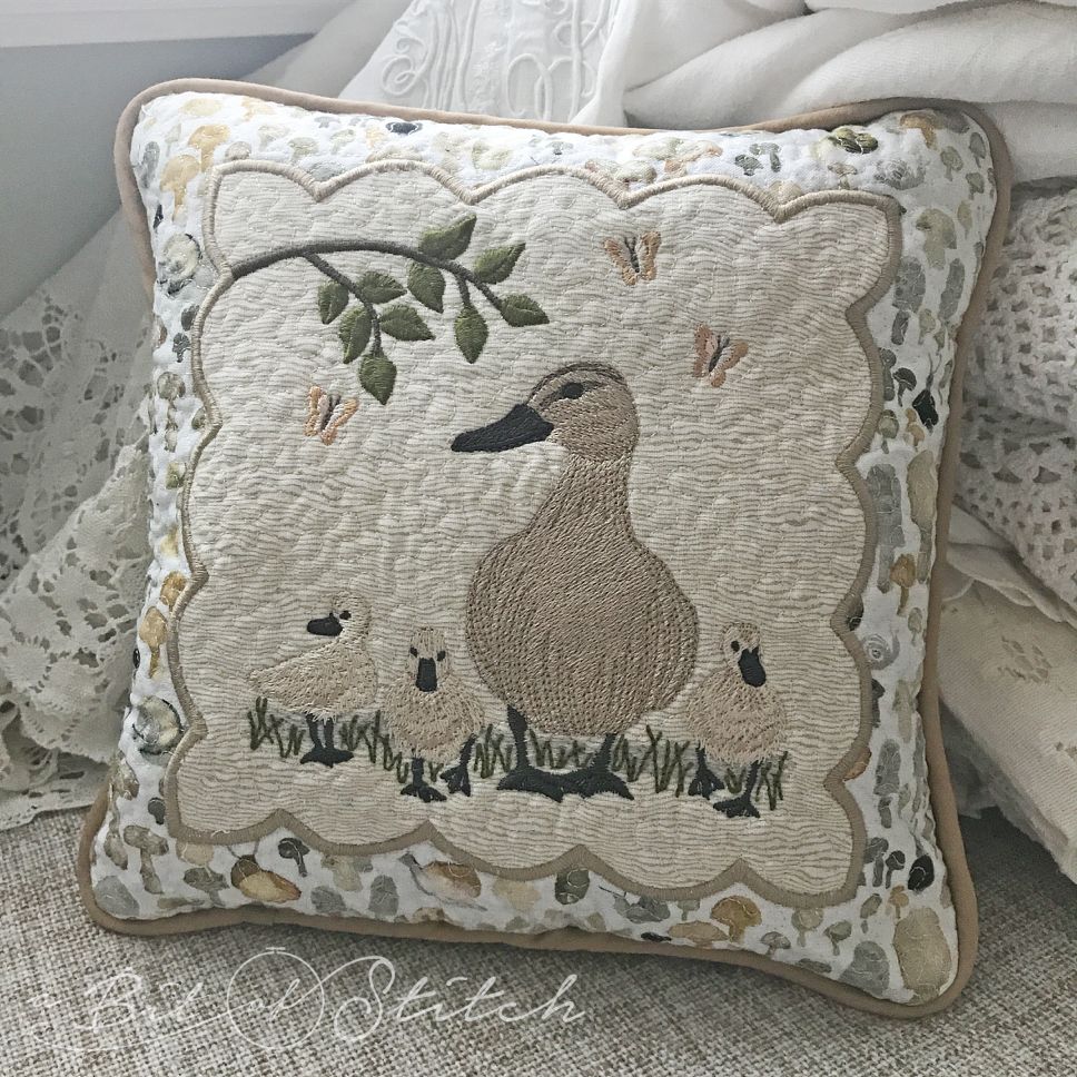 May Ducklings machine embroidery design by A Bit of Stitch - mother duck with baby ducklings, butterflies and "May" script, stitched on a decorative pillow