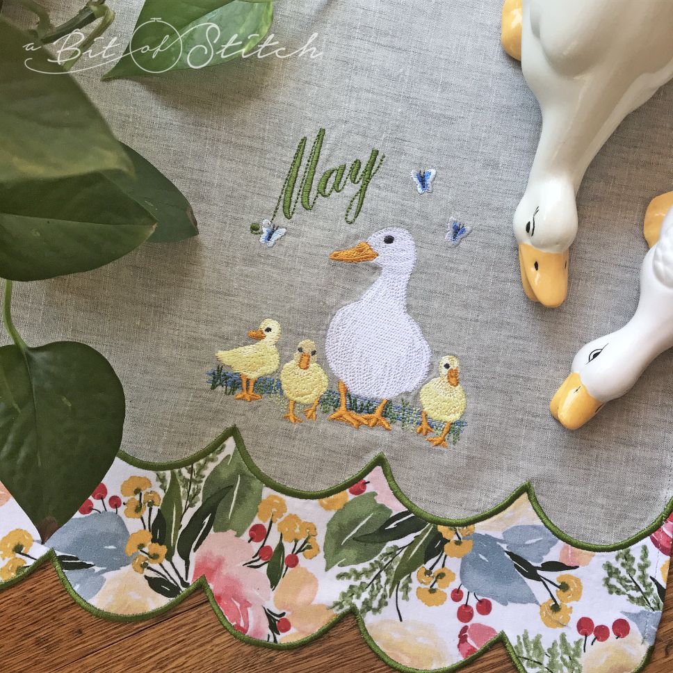 May Ducklings machine embroidery design by A Bit of Stitch - mother duck with baby ducklings, butterflies and "May" script, stitched on a tea towel with machine embroidered cutwork hem
